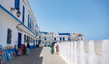 Tourists explore the scenic white and blue streets of Asilah, Morocco on a sunny day.